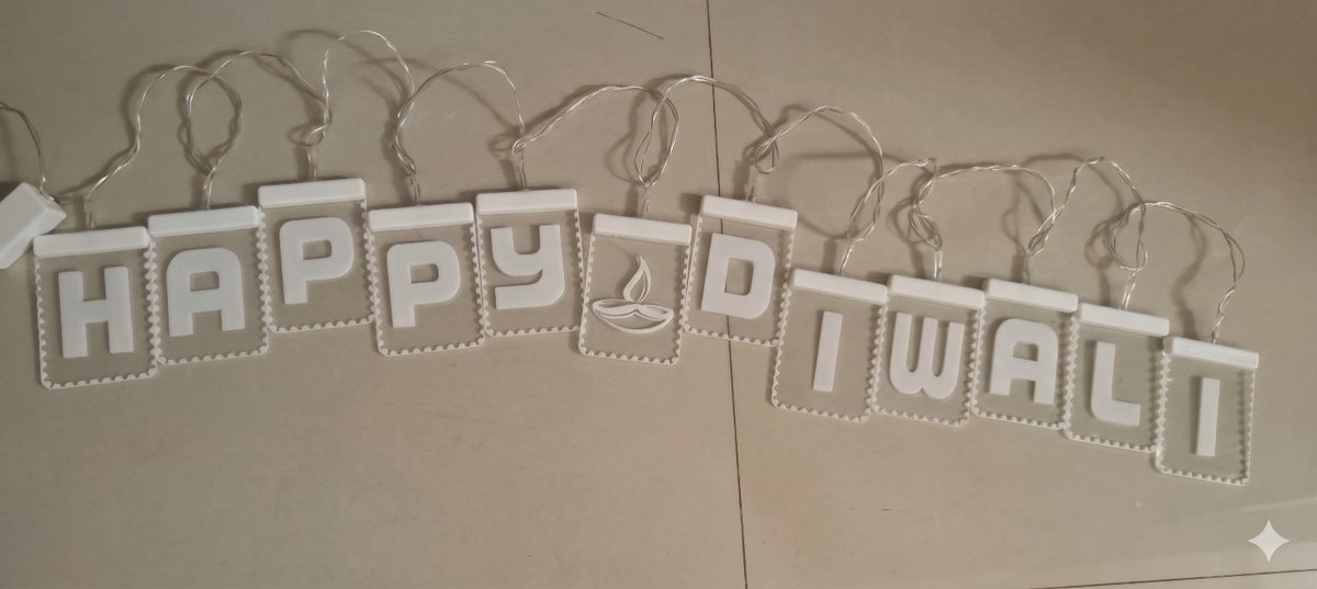 Actual product photo of a Happy Diwali letter banner with white raised letters, diya symbol, connecting wire, and power plug