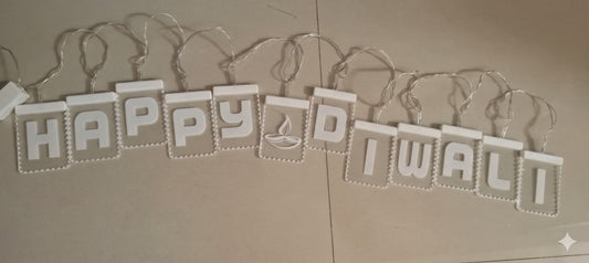 Actual product photo of a Happy Diwali letter banner with white raised letters, diya symbol, connecting wire, and power plug