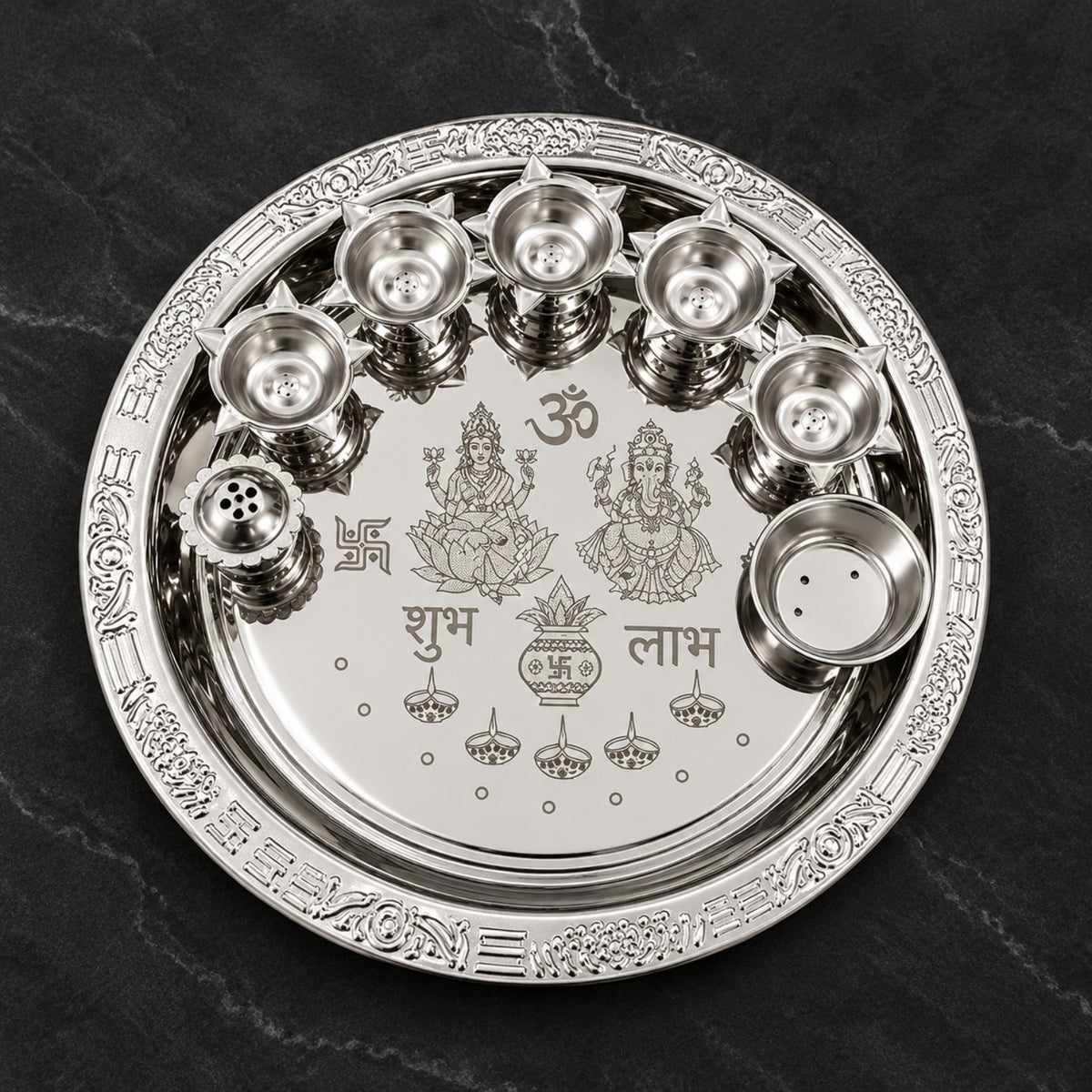 Actual product photo of a round silver-finish Lakshmi Ganesha pooja thali set with engraved devotional artwork, multiple diya cups, incense holder, and small ritual bowl on a dark background